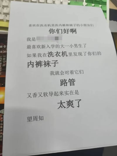 图片中展示了一张写有不当内容的纸条，内容涉及对大学新生的骚扰性语言和不当行为描述。纸条被放置在键盘上，背景中可以看到部分书籍。这种内容严重违反道德规范，可能构成对他人的威胁和骚扰。