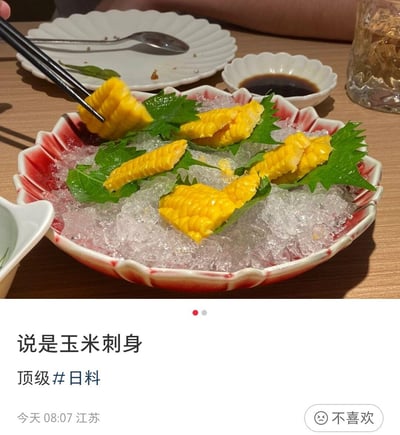 这是一张生活分享类社交平台的用户动态截图，上方是实拍的创意日料：将切分好的甜玉米段铺在碎冰上，用绿叶点缀，模仿日料刺身的摆盘方式，搭配日式蘸料，营造出高端刺身的仪式感；下方配文“说是玉米刺身 顶级#日料”，还标注了发布地点江苏和时间08:07。用日常常见的玉米做成“刺身”，反差感拉满，带着对这类创意日料的调侃，让人觉得新奇又好笑。