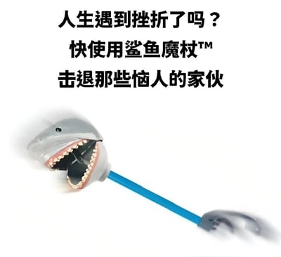 这是一张幽默风格的图片，上方配有文字'人生遇到挫折了吗？快使用鲨鱼魔杖™击退那些恼人的家伙'，下方展示了一个鲨鱼头形状的玩具，它有着张开的嘴巴和明显的牙齿，连接着蓝色的长手柄，整体设计成类似魔杖的造型，通过夸张的产品概念来幽默地表达面对生活挫折时的应对态度。