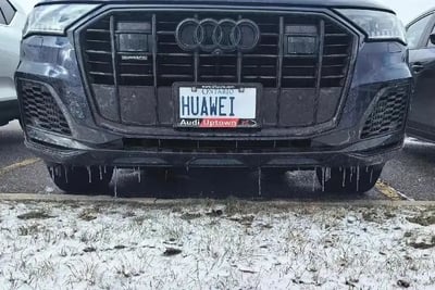 这是一张奥迪汽车前脸的照片，车牌号码十分有趣地使用了“HUAWEI”，把中国科技品牌和德国豪车巧妙联系。车主采用了自定义车牌的方式，表现出网络时代的幽默和品牌情怀。这种中西合璧的场景经常让人莞尔一笑。车子背景处于冬季的加拿大安大略省，地面与车身带有积雪和冰挂，也体现了地理及季节特色。图片没有复杂拼贴和合成，是实拍趣图。