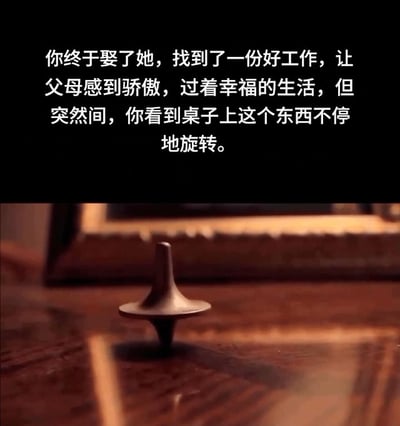 图片分为上下两部分，上半部分为黑色背景白色文字：“你终于娶了她，找到了一份好工作，让父母感到骄傲，过着幸福的生活，但突然间，你看到桌子上这个东西不停地旋转。”下半部分是一张实拍照片，展示一个金属质感的旋转陀螺在木质桌面上高速旋转，背景中隐约可见一个相框的边缘。整体通过文字营造的幸福生活与旋转陀螺的意象形成对比，暗示看似美满的现实可能如同陀螺旋转般虚幻，引人思考生活的真实性与梦境的边界。