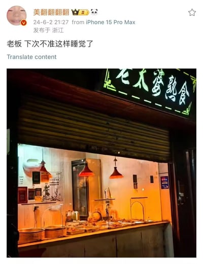这是一张社交媒体截图，用户“美翻翻翻翻”（已认证）发布了一条带有调侃意味的动态，内容为“老板 下次不准这样睡觉了”，并配上了一张熟食店的夜景照片。照片中可以看到店铺招牌“老大婆熟食”的绿色霓虹灯字样，卷帘门部分关闭，店内亮着暖黄色灯光，展示柜里摆放着各类熟食，整体氛围温馨又带点诙谐。