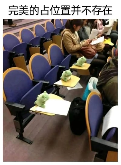 图片展示了一个阶梯教室场景，蓝色座椅搭配黄色扶手，前排多个座位的折叠小桌上摆放着绿色恐龙玩偶，疑似用于占座。背景中可见几位学生坐着阅读或整理资料。图片顶部配有文字“完美的占位置并不存在”，幽默调侃了用物品占座却可能被更“强势”方式取代的校园现象。