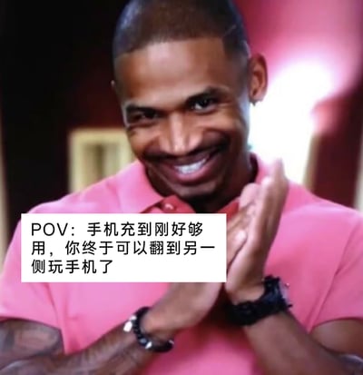 这是一张基于美剧截图制作的搞笑表情包，图中穿粉色POLO衫的黑人男性双手合十鼓掌，脸上露出开心满足的大笑表情。下方白色文字框里的文案为“POV：手机充到刚好够用，你终于可以翻到另一侧玩手机了”，精准戳中了很多人睡前因充电线限制只能固定侧身玩手机，等手机充到足够电量后，终于能自由翻身换姿势玩手机的日常小确幸，用人物开心的动作和表情放大了这种简单的快乐，十分贴合当代人的日常手机使用场景。