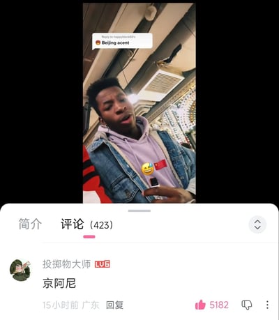 这是一张社交媒体视频的截图，展示了一位穿着牛仔夹克和紫色连帽衫的人正在说话。视频上方有文字标注"Beijing accent"，表明内容可能与北京口音相关。截图下方显示了评论区，其中一条来自用户"投掷物大师"的评论"京阿尼"获得了5182个点赞，成为热门评论。背景看起来像是在室内公共场所，可能是餐馆或商场。