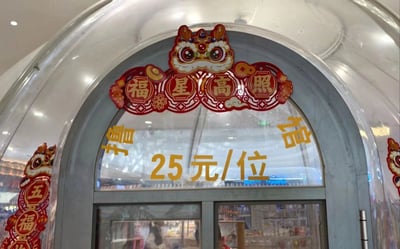 一张商场内撸猫馆的实拍照片，拱形门上装饰着醒目的春节元素。正上方是一个红色狮子头造型的装饰，下面有四个红色灯笼状的装饰，写着“福星高照”四个金色大字。门玻璃上用黄色字体写着“撸猫馆 25元/位”的价格信息。左右两侧还有红色的“五福”装饰，整体呈现出浓厚的春节喜庆氛围。