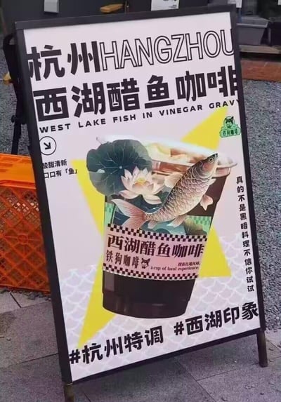 这是杭州铁狗咖啡推出的西湖醋鱼主题特调咖啡的线下宣传立牌，将杭州名菜西湖醋鱼与咖啡创意结合，打造城市特色饮品。立牌采用创意合成画面，把西湖醋鱼、荷花元素与咖啡杯结合，配文「酸甜清新，口口有「鱼」」「真的不是黑暗料理不信你试试」，并用#杭州特调 #西湖印象标签强化在地属性，吸引顾客尝试。
其中「口口有「鱼」」使用了谐音梗，谐音「口口有余」，既贴合产品主题，又带有吉祥寓意。