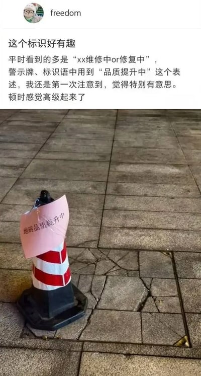 这是一张社交媒体图文帖截图，上半部分是用户freedom发布的评论内容，称往常地砖维修的警示牌大多写“维修中”“修复中”，自己第一次看到用“品质提升中”来表述维修状态，觉得这个说法很有意思，瞬间显得档次变高了；下半部分是实拍的现场图，开裂的灰色地砖路面旁立着一个红白相间的交通路锥，路锥上贴着一张粉色纸条，上面印着“地砖品质提升中”的字样。