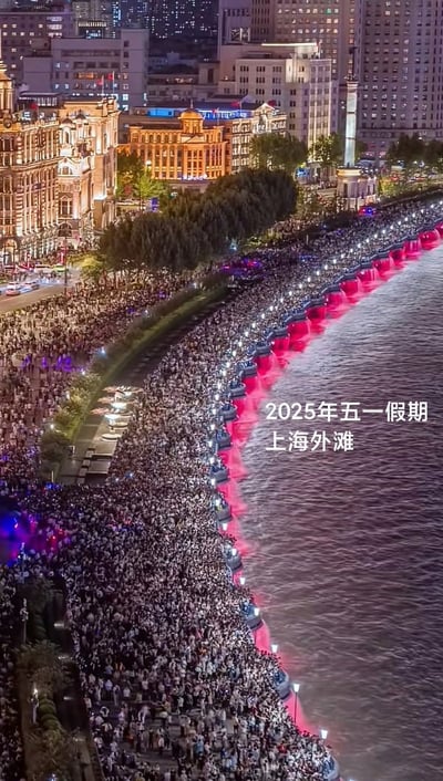 2025年五一假期期间的上海外滩夜景，大量游客聚集在黄浦江畔，人山人海。岸边建筑灯火辉煌，江面上有红色灯光装饰，展现出节假日期间上海外滩的热闹景象。