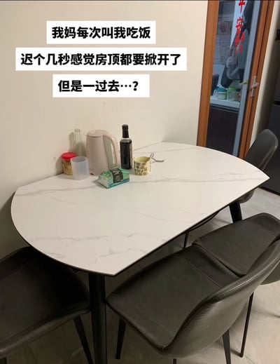 这是一张网友创作的生活吐槽实拍图，图片上方添加了三段吐槽文字，内容为“我妈每次叫我吃饭，迟个几秒感觉房顶都要掀开了，但是一过去…？”，图片主体是一张家用椭圆形餐桌，桌面上仅摆放了电热水壶、纸巾、调味瓶、水杯等杂物，没有准备好的饭菜，用这种场景反差，吐槽生活中很常见的「妈妈很早就疯狂催促孩子去吃饭，但孩子到餐桌后发现饭菜根本还没做好」的家庭日常情景。