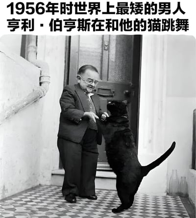 这张黑白历史照片记录了1956年时世界上最矮的男人亨利·伯亨斯与他的黑猫共舞的温馨场景。照片中，亨利·伯亨斯身着西装，戴着眼镜，正牵着站立起来的黑猫的前爪，仿佛在进行一场特别的舞蹈。背景中可以看到一扇木门和方格图案的地板，营造出年代感十足的生活氛围。