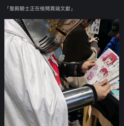 在漫展类活动现场，一位cos成圣殿骑士的爱好者正双手捧着一本二次元同人漫画册专注翻阅。图片顶部配有繁体中文文字「聖殿騎士正在檢閱異端文獻」，利用圣殿骑士原本宗教审查异端的身份，与当下翻阅ACG内容的行为形成强烈反差，制造出搞笑的违和感，调侃二次元内容被戏称为“异端文献”。
