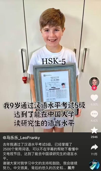 图片中是一位金发小男孩，身穿白色印有“HSK-5”字样的T恤，双手捧着镶有蓝色边框的汉语水平考试五级证书，面带灿烂微笑站在白色衣柜前。图片下方配有文字“我9岁通过汉语水平考试5级 达到了能在中国大学读研究生的语言水平”，并显示该内容在社交媒体上获得8.9万点赞、4.4万评论和7.1万分享。账号@马乐乐_LeoFranky在配文中补充，去年通过HSK五级，掌握2500个常用词，可无字幕观看中文节目，感谢网友支持并表示会继续努力学习中文。