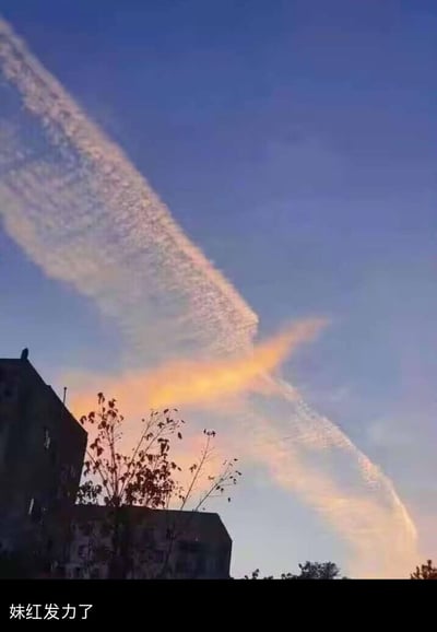 这是一张真实拍摄的天空照片，画面中一道带有彩光的长条航迹云横贯天空，被中间一块暖橙色云团“截断”，视觉上呈现出被劈开的效果。图片底部配文“妹红发力了”，玩起了东方Project系列中藤原妹红的角色梗，将自然形成的奇特云象与二次元角色的能力设定关联，营造出二次元角色打破三次元现实的趣味脑洞效果。