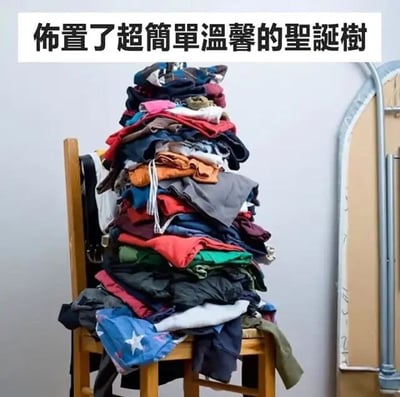 图片中，一把木质椅子上堆满了各种颜色的衣物（包括红色、蓝色、黑色、橙色等），衣物杂乱地堆叠成类似圣诞树的锥形形状。图片顶部配有文字“布置了超簡單溫馨的聖誕樹”，通过将凌乱的衣物堆比喻成“圣诞树”，形成幽默的反差效果，调侃了简化版节日装饰的创意（或无奈）。