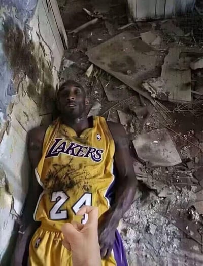 这是一张利用视觉错位手法制作的趣味梗图，将印有NBA球星科比·布莱恩特24号湖人球衣的印刷品放置在类似废墟的地面角落，拍摄者的手做出抓住球衣上“24”数字的姿势，从特定拍摄角度看，仿佛科比身处废墟墙体旁，营造出戏剧性的视觉错觉，以此制造趣味效果，图中没有双关、谐音梗或暗示内容。