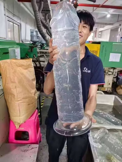 这张图片拍摄于工厂车间，一名工人手举一个超大号的透明物体，看起来像被无限放大的安全套，十分夸张搞笑。这类图片经常被网友用来调侃“巨大化”、“荒诞幽默”或作网络玩笑。图片存在明显的双关和‘尺度梗’暗示，常用以调侃或引发联想。