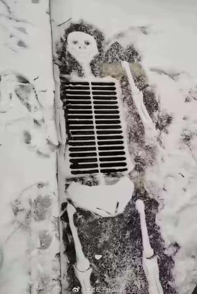 这是一张经过修改的黑白地面照片，地面上的长条排水格栅被巧妙地和添加的骷髅形象结合，营造出骷髅“嵌”在地面的视觉错觉。排水格栅恰好对应骷髅的胸腔部位，周围的深色污渍模拟出骷髅的身体轮廓，再加上绘制的骷髅头部、手臂和腿部骨骼，让整个画面看起来仿佛一具骷髅平躺着，胸腔位置正好是排水口，充满了巧合感和趣味性，给人一种猎奇又搞笑的观感。