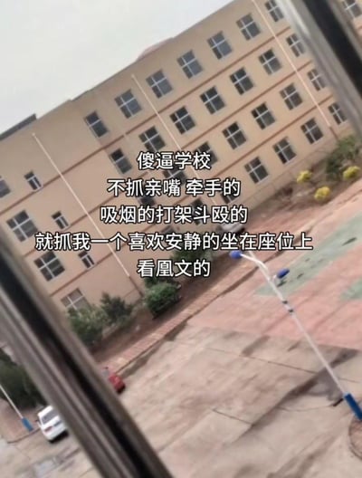 这是一张从教室窗户向外拍摄的学校室外场景实拍图，背景是学校的多层教学楼与操场区域。图中叠加了白色吐槽文字，内容为：“傻逼学校
不抓亲嘴 牵手的
吸烟的打架斗殴的
就抓我一个喜欢安静的坐在座位上
看凰文的”。其中“凰文”是谐音梗，隐晦指代低俗色情文字内容，整体表达了发布者对学校管理双标的不满与无奈，充满吐槽情绪。