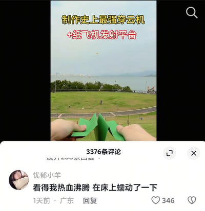 这是一张抖音短视频的截图，画面上方配有黄色和红色文字“制作史上最强穿云机+纸飞机发射平台”，前景是一双手正拿着绿色的特殊造型纸飞机，背景是开阔的滨江草坪与江景，空中还能看到已经飞出去的纸飞机。下方是视频的评论区，用户“忧郁小羊”发布评论“看得我热血沸腾 在床上蠕动了一下”，用夸张的反差感制造笑点——将“热血沸腾”的激动情绪，用“在床上蠕动一下”这种敷衍又滑稽的小动作来表现，形成强烈的搞笑反差。