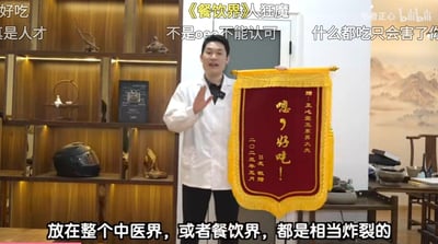 这是B站up主「医者正心」的视频截图，画面中一位身着白大褂的正心堂刘家界大夫，手持粉丝赠送的整活锦旗，锦旗上写着「嗯，好吃！」，落款为「B友敬赠 二〇二三年五月」。画面上方飘着观众的趣味弹幕：「好吃」「真是人才」「《餐饮界》人狂魔」等，底部配文「放在整个中医界，或者餐饮界，都是相当炸裂的」，将中医大夫与美食博主的反差感拉满，玩梗趣味十足，充满搞笑氛围。