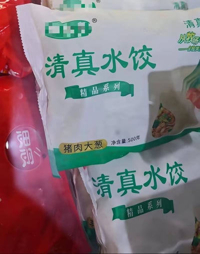 图片近距离拍摄了一袋“清真水饺”的包装袋，包装袋主体为白色，印有绿色的“清真水饺”和“精品系列”字样，下方黄色标签明确标注馅料为“猪肉大葱”，净含量500克。由于清真食品教义禁止食用猪肉，“清真”与“猪肉馅”的组合形成了明显的矛盾，画面直观展现了这一荒谬的产品标签错误，充满了反差感和荒诞意味。
