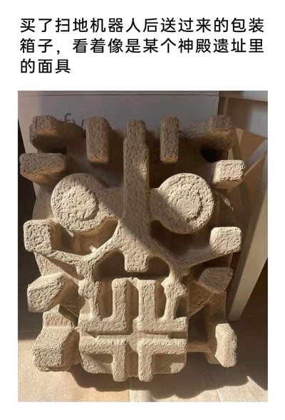 这是一张图文结合的实拍图片，上方配有文字说明，指出图中物品是购买扫地机器人时附带的纸浆缓冲包装。这个包装的造型十分独特，中间的凸起结构与孔洞组合后，形成了类似有着圆形大眼、造型古朴的远古神殿面具的外观，表面的粗糙纹理加上光影的衬托，进一步强化了这种复古神秘的视觉效果，是生活中偶然发现的趣味视觉巧合。