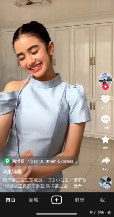 这是一张竖屏短视频平台的截图，画面主体是柬埔寨王室的13岁小公主诺罗敦·珍娜。她身着浅蓝色露肩礼服，头发盘起，正闭眼展露甜美笑容，双手做出轻拍的动作，神态十分愉悦。背景是室内的白色储物柜，截图右侧展示了该视频的互动数据：3465个点赞、1148条评论、186个收藏、493次转发。图中的文字内容介绍了她的柬埔寨王国王室成员身份，称她多才多艺。右下角带有知乎用户@胡不喜的水印，说明该截图在知乎平台也有传播。