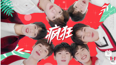 这是肯德基的品牌宣传物料截图，画面以鲜艳的大红色为背景，时代少年团的七位成员围绕着中间醒目的白色书法字体“疯狂”呈环形排列，成员们均面带灿烂笑容看向镜头，整体氛围活泼热烈，旨在为肯德基的相关产品或活动进行宣传，图中无谐音梗、双关等特殊内容。