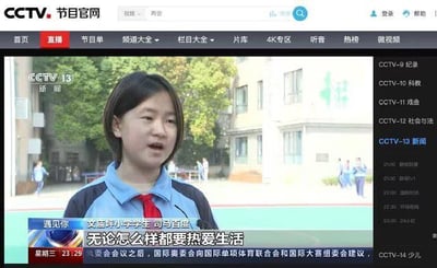 这是一张CCTV节目官网的直播页面截图，展示的是CCTV13新闻频道《遇见你》栏目的采访内容。画面主体是身着蓝黑相间校服、系着红色红领巾的文庙坪小学女学生司马百度，她身处校园户外场景中，正在面对镜头接受采访。画面下方字幕标注了受访者身份和她的发言“无论怎么样都要热爱生活”，页面顶部是CCTV节目官网的导航栏，右侧罗列了央视各频道列表及对应节目单，左下角显示当前时间为星期三23:29，页面底部还有滚动的其他新闻快讯字幕。