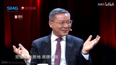 这是东方卫视政论节目《这就是中国》的视频截图，学者张维为身着西装、佩戴眼镜，面带温和笑容，双手摊开手掌向上，正激昂地说出“完全地 大胆地 放肆地做”这句话，姿态与神情传递出充满力量的鼓励感，适合用来表达支持他人放开手脚行动的语境。