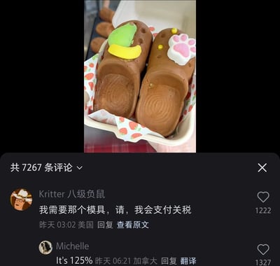 这是一张竖屏的社交媒体截图，画面上半部分是一对以流行洞洞鞋为原型制作的巧克力甜点，甜点为棕色，表面还原了洞洞鞋的孔洞和鞋底纹理，还分别装饰了绿黄配色的仿真鞋花和粉白爪印造型的装饰，被放置在印有草莓图案的包装纸和白色餐盒中。画面下半部分是该内容的评论区，显示共有7267条评论，其中两条热门评论分别来自美国用户“Kritter 八级负鼠”和加拿大用户Michelle，前者表示想要制作这款甜点的模具，愿意支付关税，获得1222个赞；后者用英文评论“It's 125%”，获得1327个赞，体现了网友对这款创意甜点的喜爱与关注。