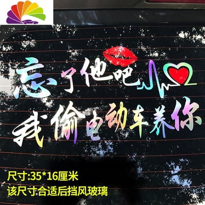 这是一张汽车后挡风玻璃贴纸的图片，上面有彩色渐变文字写着'忘了他吧 我偷电动车养你'，配有红唇印和心形图案。底部有黄色文字标注尺寸信息'35*16厘米 该尺寸合适后挡风玻璃'。这是基于广西偷车男经典语录创作的网络梗商品，通过将违法行为包装成荒诞承诺的方式制造幽默效果，体现了网民的自嘲精神和创造力，成为表达经济压力的幽默方式。