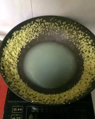 这是一张生活化的搞笑图片，显示一个炒锅，锅边围满了蒜蓉，中间却留着一块空白。这通常暗示做饭的人在炒菜时掌控锅铲的技术不过关，导致蒜蓉都甩在了锅的边缘，画面充满自嘲的幽默气氛。这种现象也常用来形容“手残党”在厨房翻车的窘态，经常在朋友圈、微博被网友晒出来调侃自己厨艺差。

暗示自嘲、幽默、生活小尴尬，带有一种‘做饭失败’的无奈感。