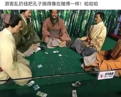 这是一张拍摄于展馆的照片，展示了一组孔子与弟子围坐讲学的蜡像场景：蜡像们围坐在绿色的台面旁，背景是模拟的竹林，原本庄重肃穆的历史讲学场景，因为游客在台面上乱扔了大量纸币，使得整个画面看起来如同几个人围坐在一起赌博，充满强烈的滑稽反差感。图片顶部配有吐槽文字“游客乱扔钱把孔子搞得像在赌博一样！哈哈哈”，右下角还有“请勿触摸 DON'T TOUCH”的警示标识，进一步凸显了场景原本的严肃性与游客不文明行为造成的滑稽效果之间的冲突，画面没有双关或谐音梗，完全是场景错位带来的搞笑反差。