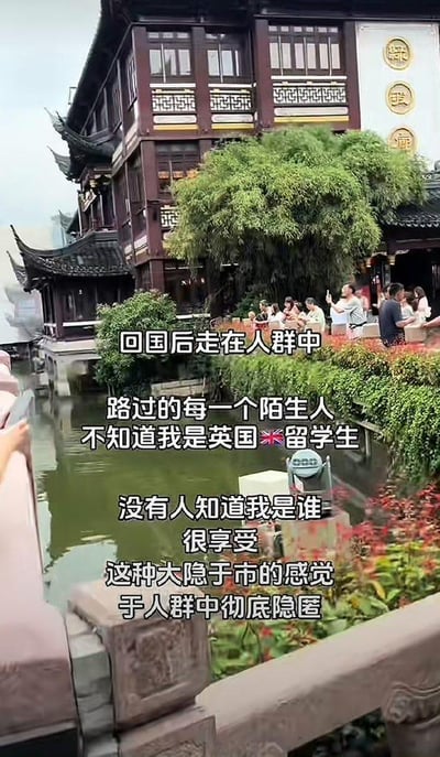 这是一张竖屏实地拍摄图，背景是上海豫园的中式传统水乡建筑，河道旁有不少游客在休闲活动，前景是石制栏杆。图中叠加了一段表达个人心境的文字，内容为：“回国后走在人群中
路过的每一个陌生人
不知道我是英国🇬🇧留学生
没有人知道我是谁
很享受
这种大隐于市的感觉
于人群中彻底隐匿”，传递出这位英国留学生回国后，回归普通人群、不被特殊标签定义的轻松惬意心境。