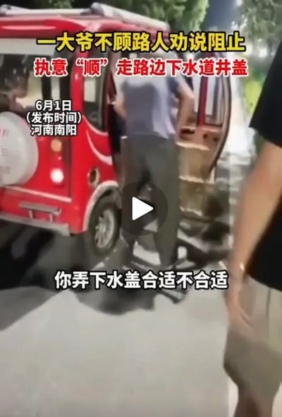 这是2024年6月1日发布于河南南阳的视频截图，画面中一位大爷正将路边的下水道井盖往自己的红色三轮车上搬运，旁边的路人见状出声劝阻：“你弄下水盖合适不合适”，但大爷无视路人的阻止，执意要拿走公共的下水道井盖。这种行为不仅侵占了公共财物，还会给过往行人和车辆带来极大的安全隐患，容易引发摔倒、车辆卡陷等事故。
