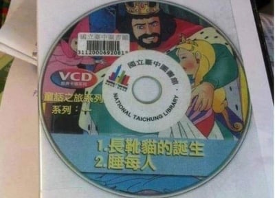 这是一张国立台中图书馆馆藏的童话系列VCD盘面的翻拍图，属于「童话之旅系列」，盘面上标注包含《长靴猫的诞生》和《睡每人》两个童话故事。其中「睡每人」是经典童话《睡美人》的错别字，形成了滑稽的笑点。盘面上还印有国王与公主的卡通形象，以及VCD标识、国立台中图书馆的中英文名称和馆藏条码等信息。

图中存在错别字梗：将「睡美人」误印为「睡每人」，因字形相近产生搞笑效果。