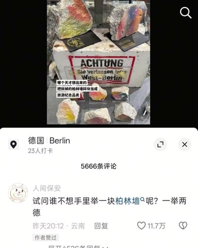 这是一张社交媒体截图，上半部分是德国柏林的纪念品售卖场景：多块被涂上彩色的柏林墙碎块被当作商品摆放，下方的展台上印有德语“注意 你正离开西柏林”的标识，配文吐槽“哪个天才想出来的 把拆掉的柏林墙碎块当成 旅游纪念品卖”；下半部分是中文社交平台的互动区，定位显示为德国柏林，有23人打卡，总评论数5666条，用户“人间保安”发表评论玩谐音梗，将成语“一举两得”改为“一举两德”对应两德统一的相关历史，该评论获11.7万赞还被作者点赞，引发大量关注。