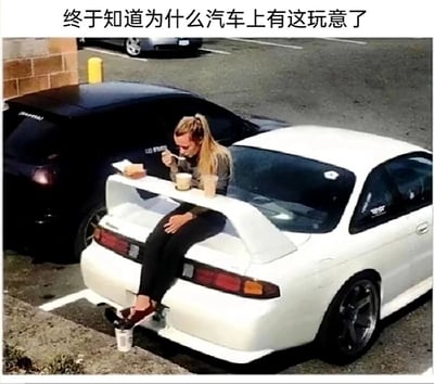 这张图片呈现了一个充满趣味的停车场场景：一位金发女子坐在一辆白色改装轿车的车尾翼上，将原本用于提升车辆行驶空气动力学性能的尾翼，当作临时餐桌使用，上面摆放着餐盒与两杯饮品，女子正手持叉子进食，同时还将一个杯子挂在车尾的拖车钩上。图片上方的配文“终于知道为什么汽车上有这玩意了”，用调侃的语气，给汽车尾翼赋予了完全脱离其设计初衷的“新功能”，通过这种反差感制造出搞笑的效果，展现了生活中充满创意的趣味瞬间。
