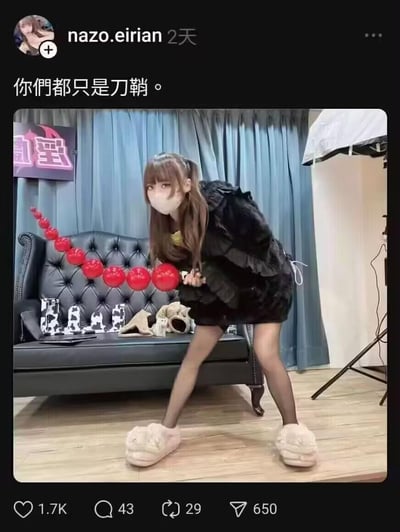 社交媒体用户nazo.eirian发布的一张个人照片，照片中女孩身着黑色毛绒外套、黑色丝袜和白色毛绒拖鞋，手持一串红色球状道具，在蓝色窗帘和黑色皮沙发的工作室背景前摆出弯腰姿势。图片上方配有文字“你們都只是刀鞘。”，整体风格带有搞怪和神秘气息，可能用于社交媒体个人动态分享或 meme 创作。