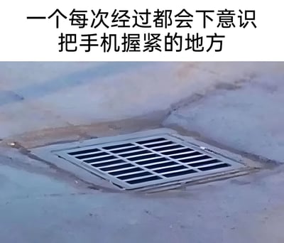 图片上方有一行文字："一个每次经过都会下意识把手机握紧的地方"，下方是一张地面排水口的照片。排水口为方形金属格栅结构，安装在灰色水泥地面上，格栅缝隙看起来足以让手机掉落。这张图通过幽默的方式表达了人们在经过类似排水口等可能导致手机掉落的地方时的本能反应，引发观众共鸣。