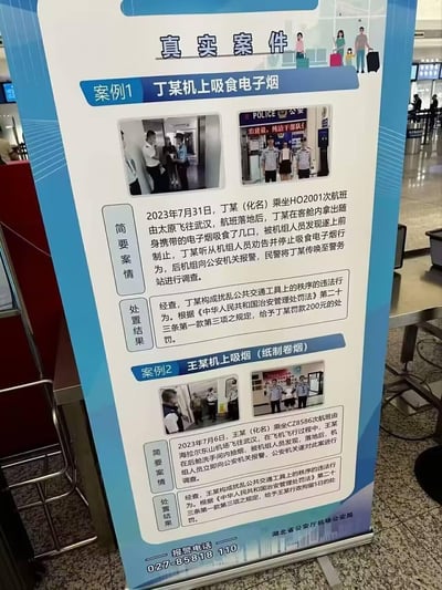 这是湖北省公安厅机场公安局设置在机场的普法宣传展架，通过两个真实违法案例警示乘客机上吸烟属于违法行为：<br>1. 2023年7月31日，丁某在吉祥航空HO2001次航班落地后吸食电子烟，被机组劝阻后报警，最终被处以200元罚款；<br>2. 2023年7月6日，王某在南方航空CZ8586次航班飞行过程中，在后舱洗手间抽纸烟，落地后被公安机关调查，最终被处以5日行政拘留。<br>展架还标注了报警电话，明确引用《中华人民共和国治安管理处罚法》相关条款，严肃传递维护民航秩序的要求。