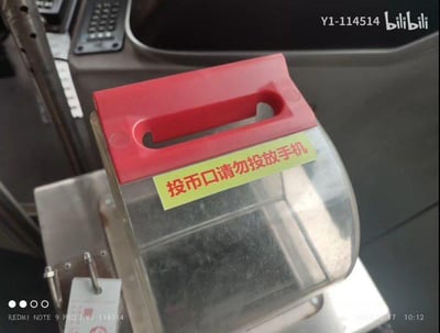 这是一张拍摄于公交车内的照片，主体是公交车的投币装置，装置的透明外壳上贴有一张黄底红字的提示标语：“投币口请勿投放手机”。正常情况下乘客不会将手机投入投币口，这个特殊的提示推测是因为曾经出现过乘客误将手机投入投币口的情况才设置的，既体现了工作人员的无奈，也让看到的人觉得有些好笑。