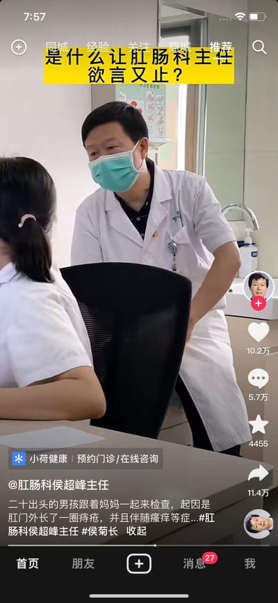 这是抖音平台的一段医疗科普视频截图，画面中肛肠科侯超峰主任（被戏称“侯菊长”，是“侯局长”的谐音，对应肛肠科相关戏称）面对一位二十出头、跟着妈妈来就诊的男孩，男孩因肛门外长痔疮且伴随瘙痒症状来检查。主任身体前倾，一只手放在身后，神情略显尴尬、欲言又止，推测是因为患者与母亲一同前来，部分隐私病情不便直接说明。该视频用于肛肠健康科普，附带小荷健康的门诊预约/咨询入口，获得了10.2万点赞、5.7万评论等较高的互动数据，通过有话题性的场景吸引用户关注肛肠健康。