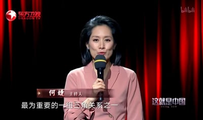 这是东方卫视政论节目《这就是中国》的录制画面截图，主持人何婕身着粉色西装，手持麦克风，正专注地进行发言，画面下方的字幕显示她正在提及“最为重要的一组三角关系之一”。背景为红黑配色的幕布，整体场景正式专业，凸显节目严肃讨论的氛围。