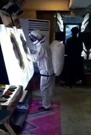 一名身穿全套防护服、背着背包的人正在街机厅中与一台大型街机游戏机互动，似乎在用手触摸或按压游戏屏幕。画面左侧可见街机的控制按钮，背景中还有另一台街机和模糊的人影。
