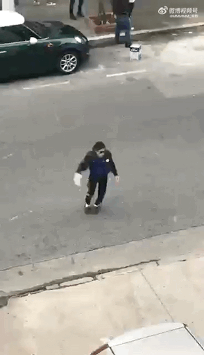 这是一段趣味动态GIF，画面中一位身着深色外套的小孩在城市街道的路面上前行，由于拍摄角度的巧合，小孩脚下的滑板被遮挡，制造出仿佛双脚悬空“悬浮”移动的视觉错觉。背景可见一辆墨绿色小型轿车与路边的行人，整个场景充满生活化的趣味性，让人忍俊不禁。