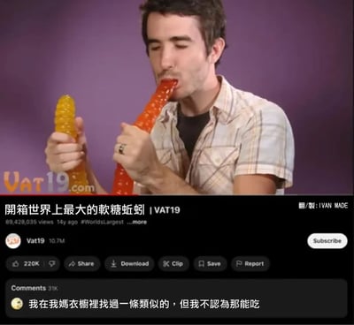 图片展示了一名男子在紫色背景前手持两条巨型软糖蚯蚓（黄色和红色），正将红色软糖蚯蚓放入口中品尝。画面下方是类似YouTube视频的界面元素，包括标题“开箱世界上最大的软糖蚯蚓 | VAT19”、8900多万次观看量、14年前上传的信息，以及Vat19频道的1070万订阅量。评论区有一条搞笑评论：“我在我媽衣櫃裡找過一條類似的，但我不認為那能吃”，通过联想制造幽默效果。