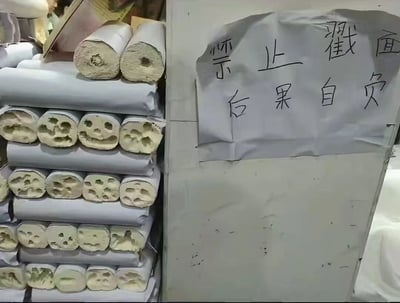 图片左侧展示了堆叠整齐的圆柱形面团，外层包裹着白色油纸，截面露出多孔的内部结构，疑似手工面食原料；右侧是一张贴在墙上的手写告示，纸张边缘略显褶皱，用黑色马克笔书写着“襟止戳面 后果自负”（其中“襟”为错别字，正确应为“禁”）。整体场景像是 bakery 或手工面馆的后厨/柜台角落，告示中严肃的警告语气与“戳面团”这一轻微行为形成反差，加上错别字的诙谐感，让日常场景充满喜剧效果。